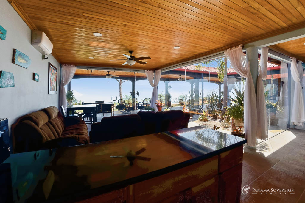 Open concept living room with wood ceiling, glass walls, and ocean view terrace in Bucaro Panama home