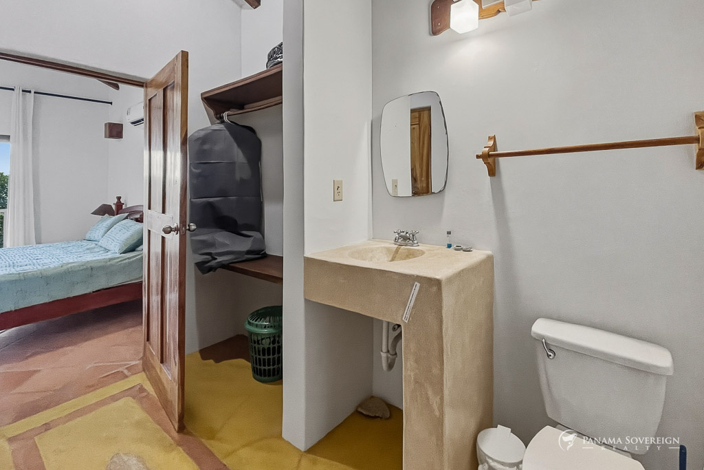 Baño con lavamanos de concreto, espejo sencillo y área de closet abierto contigua