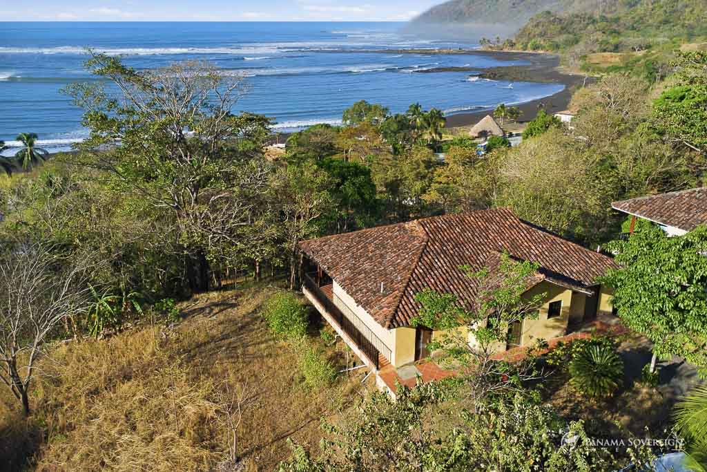 Propiedad con vista al mar, casa principal rodeada de árboles y costa curva visible