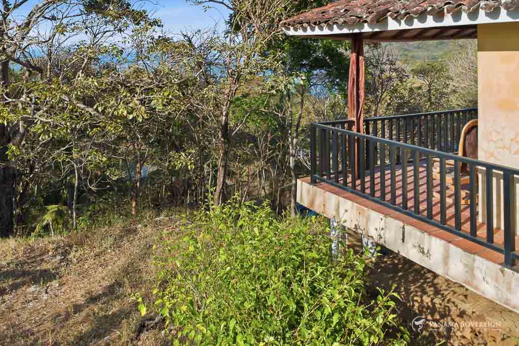 Terraza exterior con baranda de madera y vista parcial al océano entre árboles