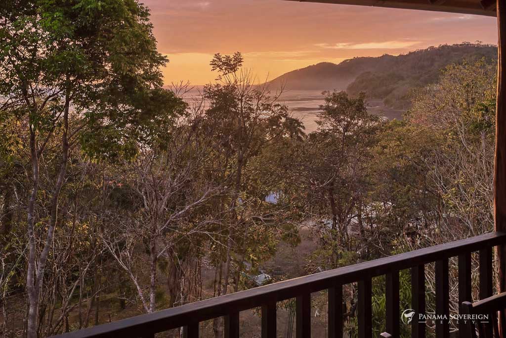 Vista al atardecer desde terraza con árboles en primer plano y océano al fondo