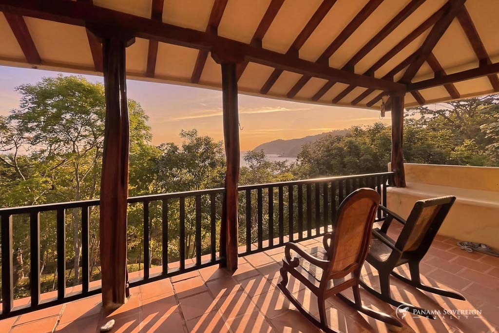 Terraza techada con mecedoras de madera y vista al océano durante el atardecer