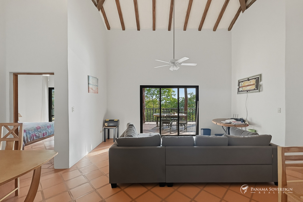 Sala con techo alto, vigas de madera, sofá y puertas corredizas hacia terraza
