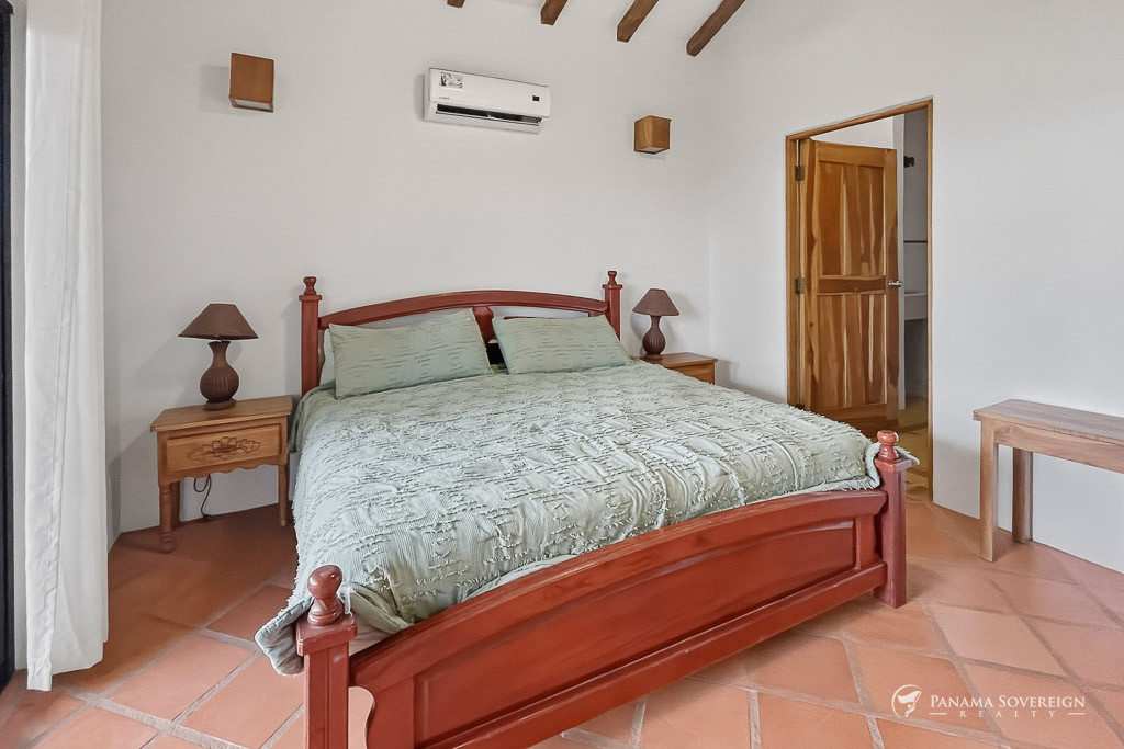 Dormitorio amplio con cama de madera, aire acondicionado y acceso a baño o vestidor