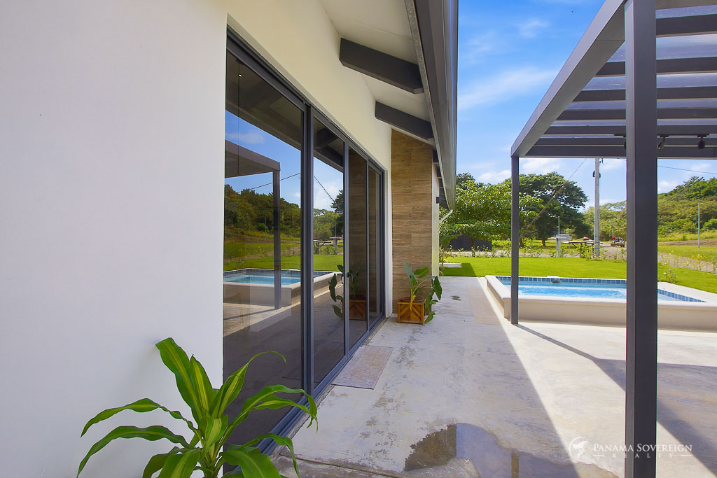 Terraza exterior moderna con pérgola, piscina pequeña, puertas corredizas de vidrio y jardín con vegetación tropical