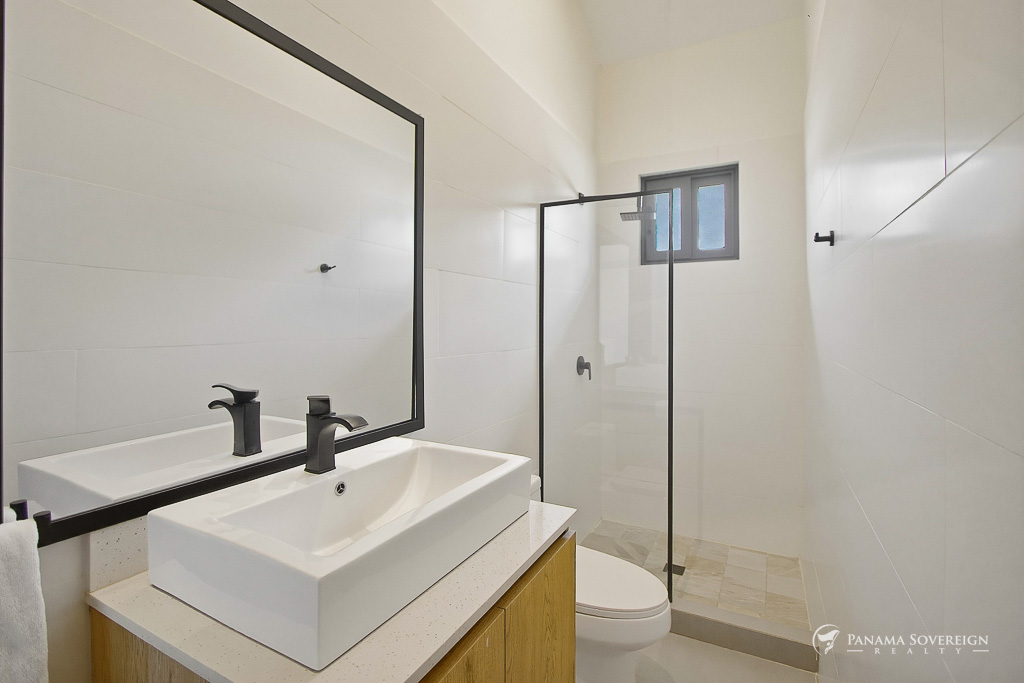 Baño moderno con doble lavamanos, grifería negra, espejo amplio, ducha de vidrio y acabados blancos limpios