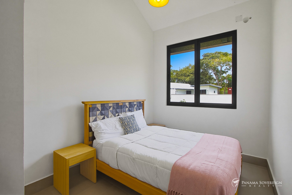 Dormitorio compacto con cama individual, mesa de noche de madera, ventana con vista a vegetación y diseño sencillo