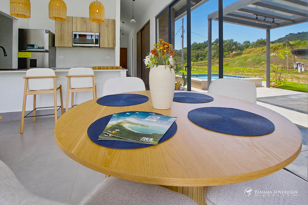 Comedor con mesa redonda de madera, decoración central, acceso a terraza y vista a piscina y jardín