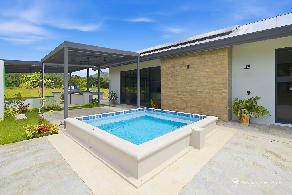 Vista lateral de la casa con amplio jardín, diseño moderno, techo metálico y acceso a piscina