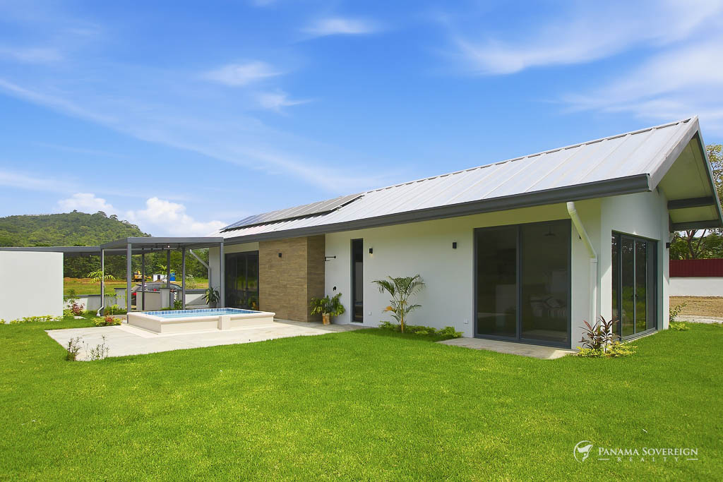 Vista trasera de la propiedad con jardín amplio, piscina, ventanales y entorno natural con colinas