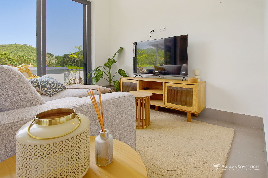 Sala acogedora con sofá de tela, mueble de TV de madera, televisor de pantalla plana y puertas corredizas hacia área verde