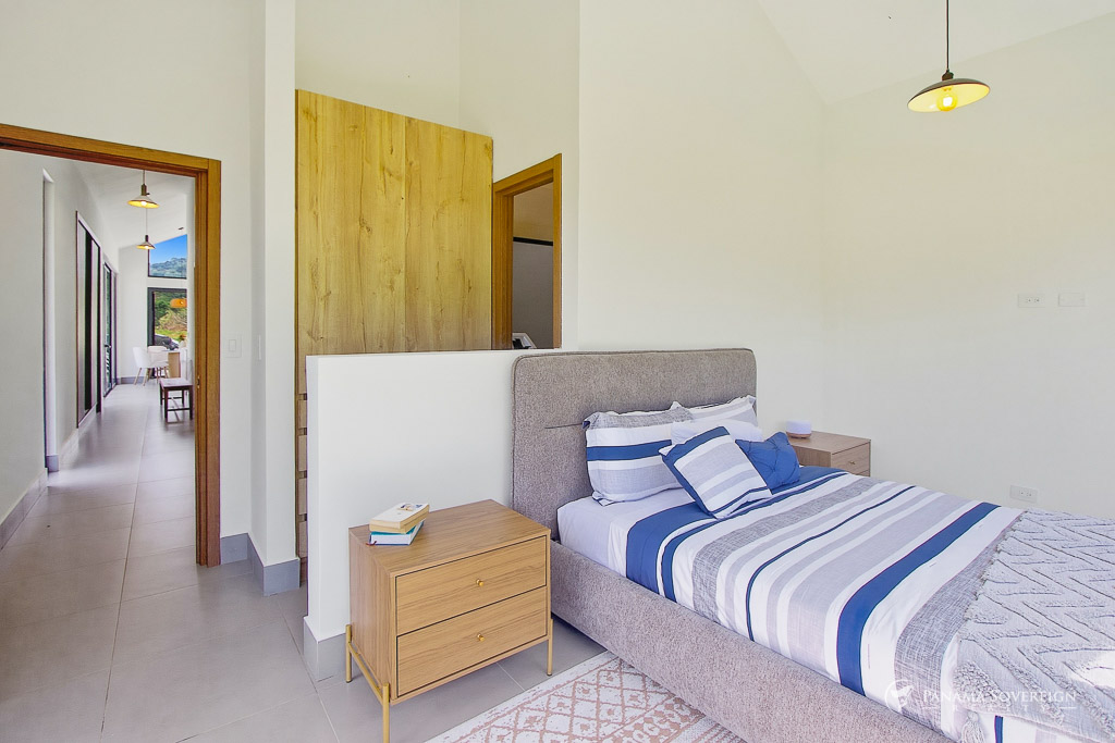 Dormitorio minimalista con cama tapizada, mesas de noche de madera, techos altos y conexión al área principal