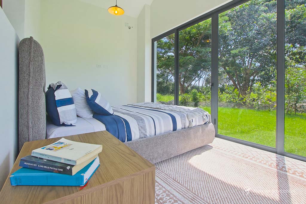Segundo dormitorio con puertas corredizas de vidrio, abundante luz natural, vista a vegetación y detalles en madera