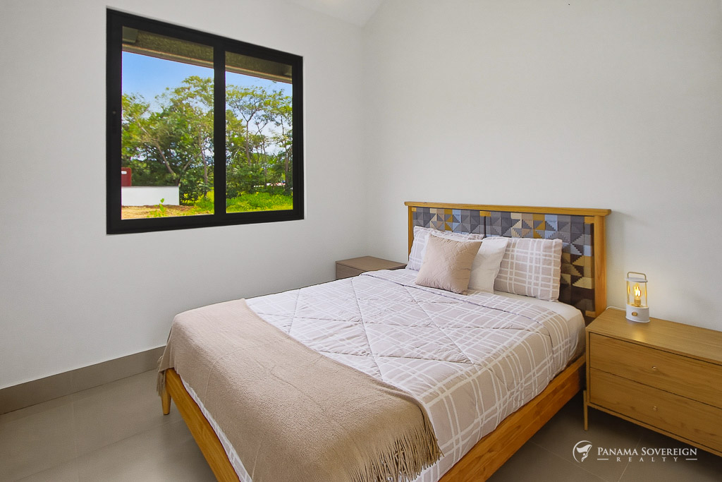 Dormitorio con ventana hacia áreas verdes, muebles de madera, ropa de cama en tonos neutros y diseño sencillo
