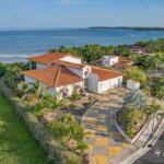 Side angle of the home revealing elegant architecture, ocean backdrop, and manicured tropical landscaping along the driveway.