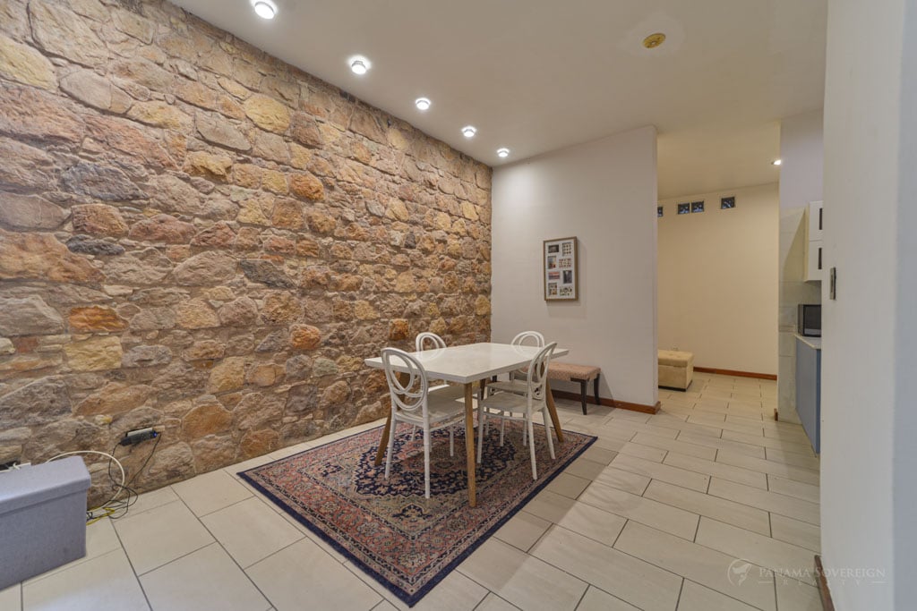 Dining area in a condo in Casco Viejo with a white table and chairs, accented by a textured stone wall, adding rustic charm to the space.