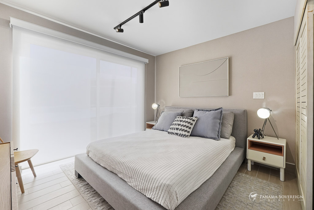 Primary bedroom with a large bed, minimalist decor, and soft natural light filtering through sheer blinds.