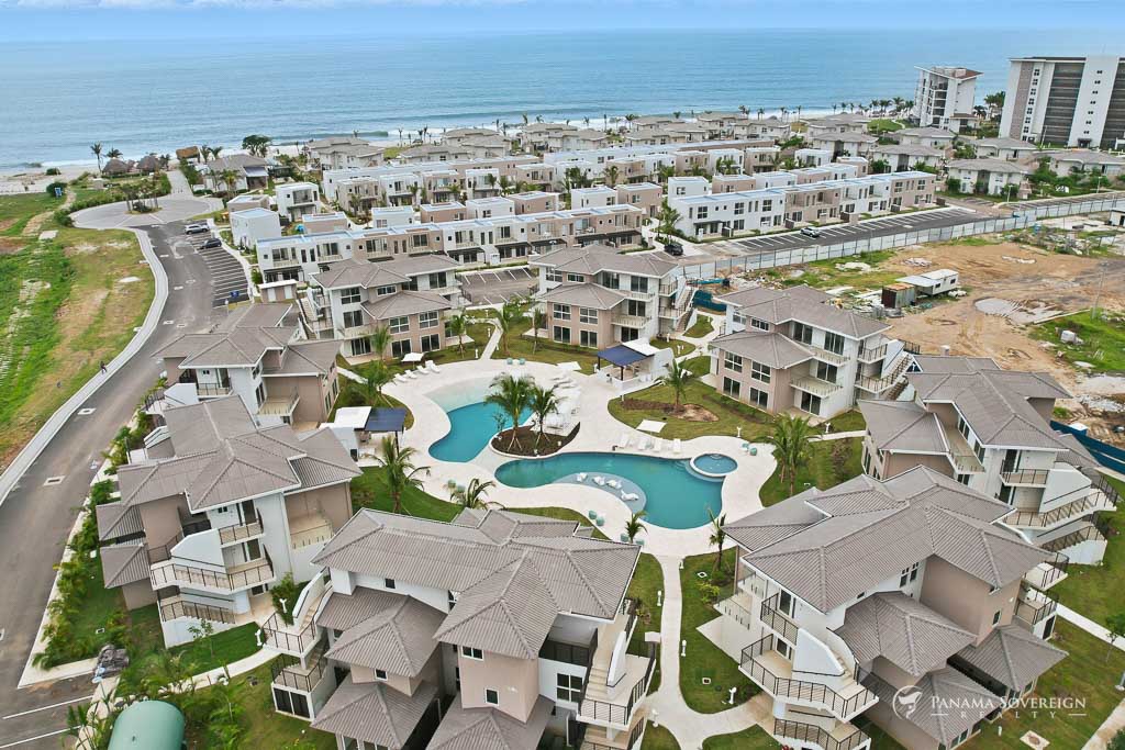 Panoramic shot showing the pool area, modern buildings, and the ocean in the distance.