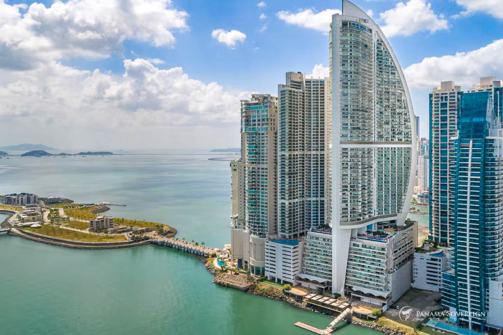 Vista exterior de un rascacielos de lujo de arquitectura moderna, situado frente al mar y rodeado de zonas verdes.