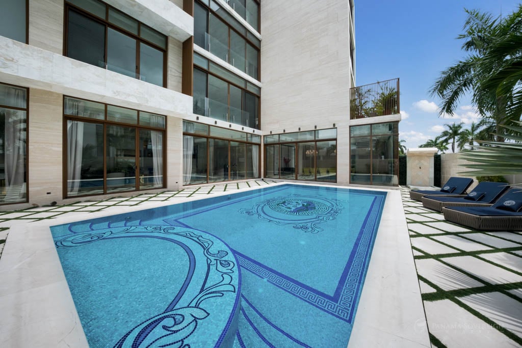 A stylish pool area with intricate designs on the pool tiles, surrounded by a modern luxury home with floor-to-ceiling windows.