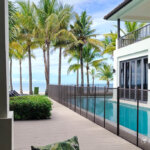 Poolside deck with safety fence, ocean view, and lush tropical landscaping.