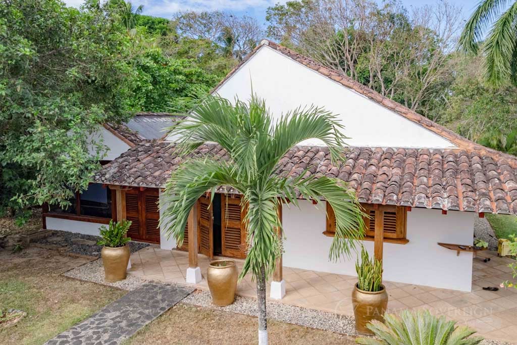 Front view of a rustic-style house with a palm tree in the foreground and wooden shutters adding to the cozy appearance.