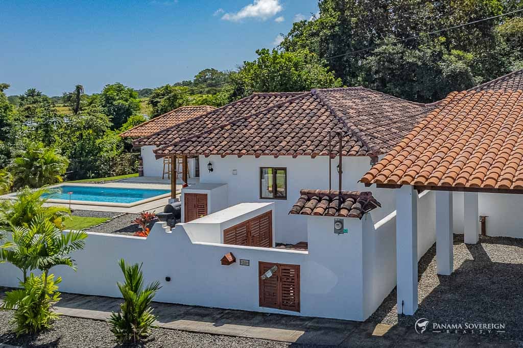 Close-up of the house exterior, featuring its white walls, terracotta tiled roof, and glimpses of the pool and garden.