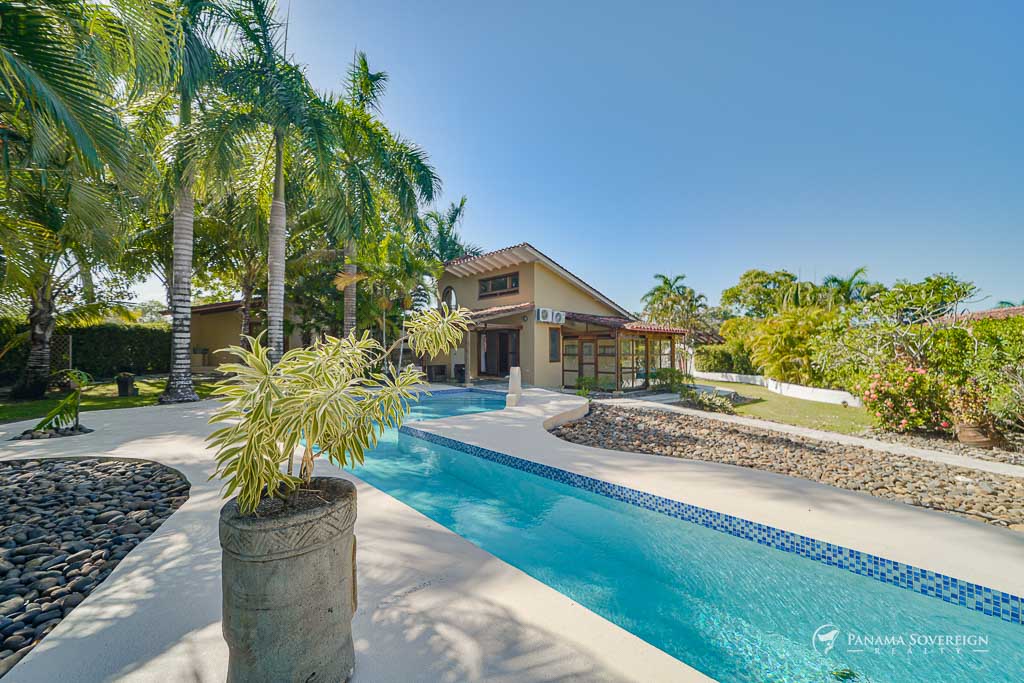 Vista completa del exterior de la casa con piscina y exuberante vegetación.