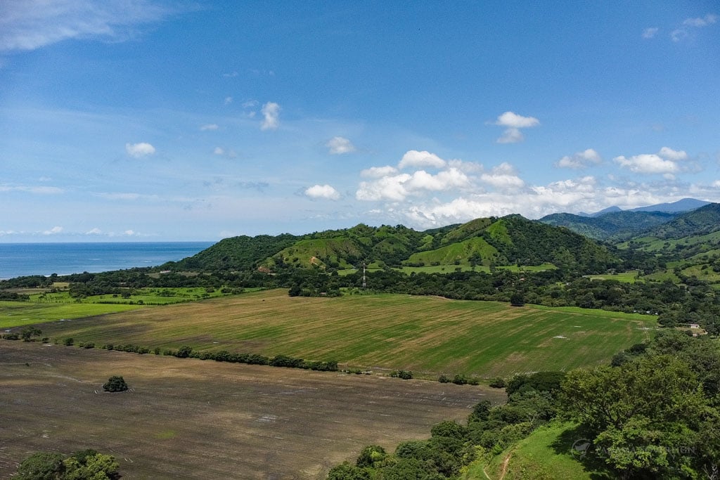 A broad aerial view of the green valleys and hills, with cultivated fields in the foreground and the ocean stretching into the horizon.