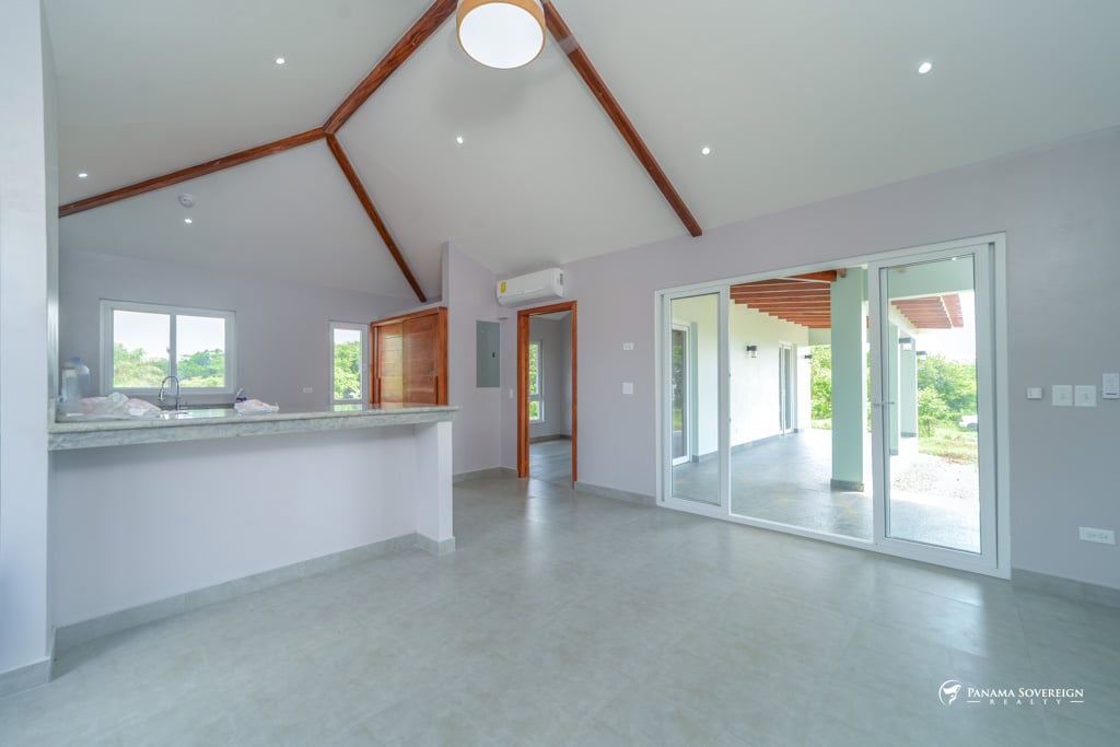 Open living area with high vaulted ceilings, large windows, and sliding glass doors leading to a covered outdoor patio