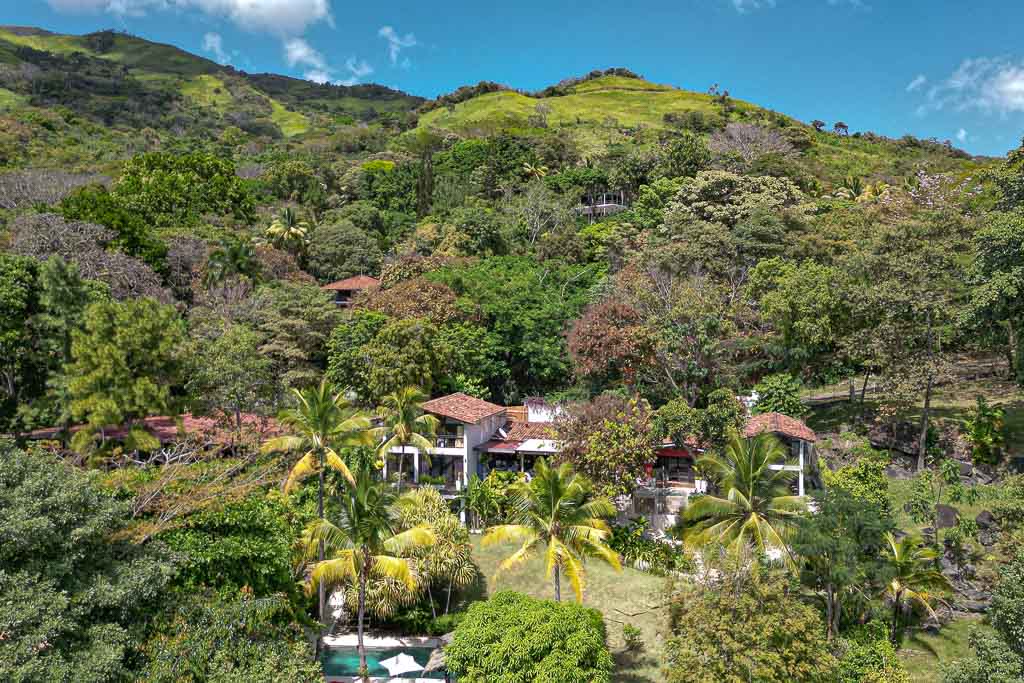 Aerial view of a luxurious property nestled in lush greenery on a hillside near Veracruz, Panama, featuring a spacious villa surrounded by tropical foliage and vibrant landscapes under a clear blue sky.